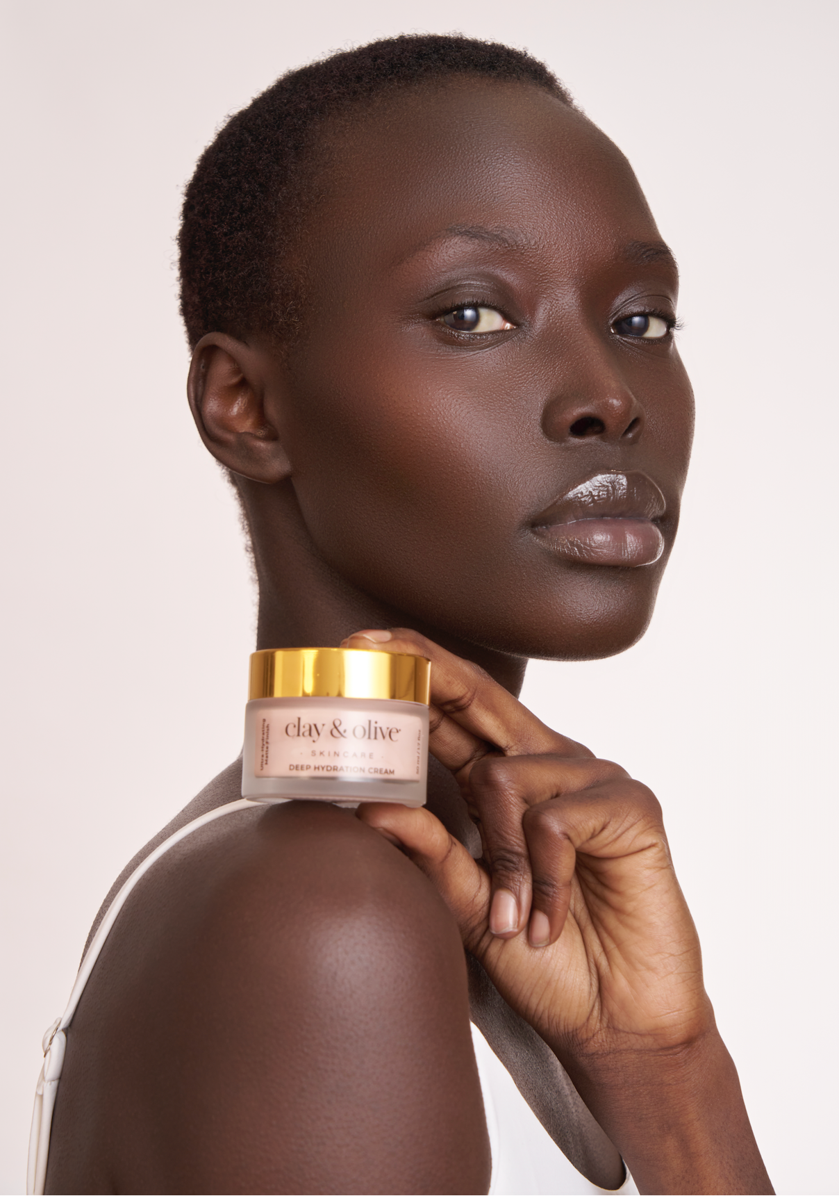 Woman holding a jar of cream against a plain background. Clay & Olive